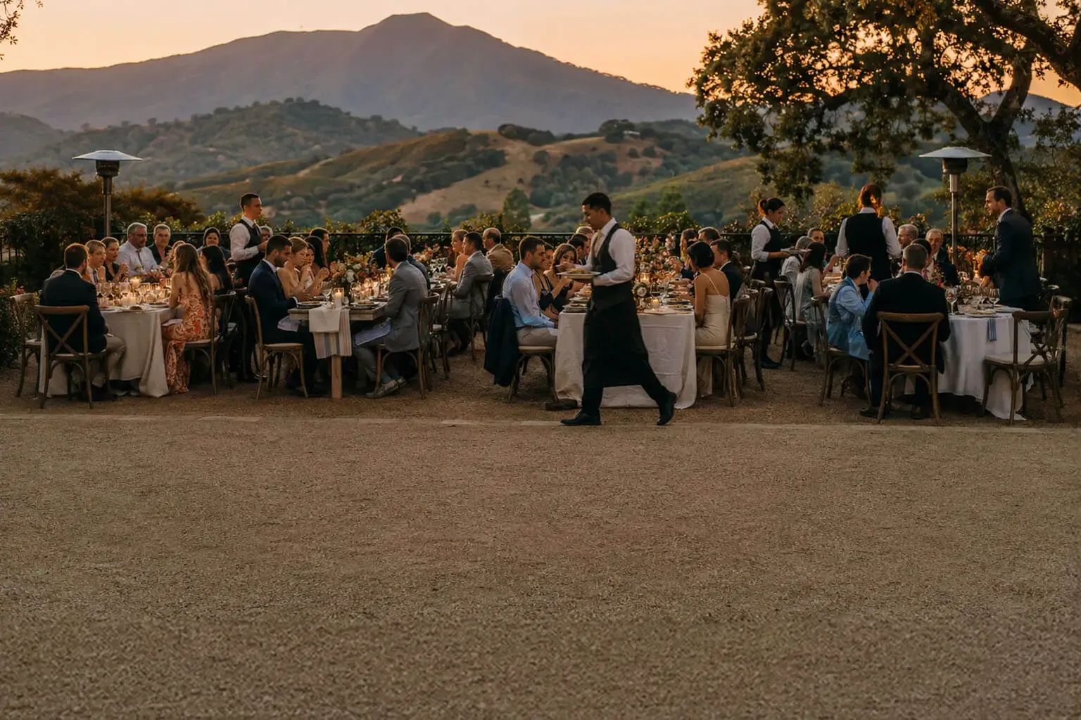 Wedding catering in Marin County, CA by Marin Catering Company — staffed reception dinner service, rentals, floral tablescapes, cake service and bar service for weddings in San Rafael, Mill Valley, Tiburon, Sausalito, Corte Madera and Novato Sunset wedding reception on a Marin County hilltop terrace — guests dining at long linen tables while catering attendants pass plated courses, with Mount Tamalpais and the golden Marin hills behind them
