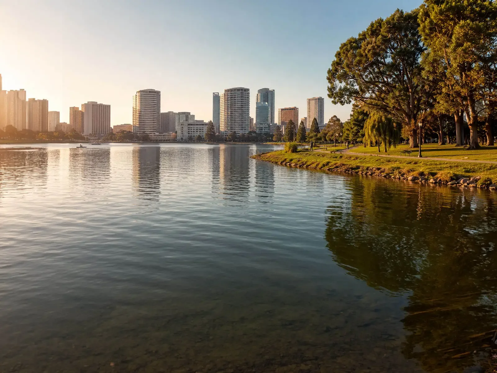 Oakland Catering Company — full-service catering around Lake Merritt and downtown Oakland, with on-site staff, setup, service and cleanup in Oakland, Berkeley, Alameda, Emeryville, Piedmont and San Leandro Golden-hour view across Lake Merritt with the downtown Oakland skyline and lakeside park path behind it — the East Bay area Oakland Catering Company serves with full-service wedding and corporate catering