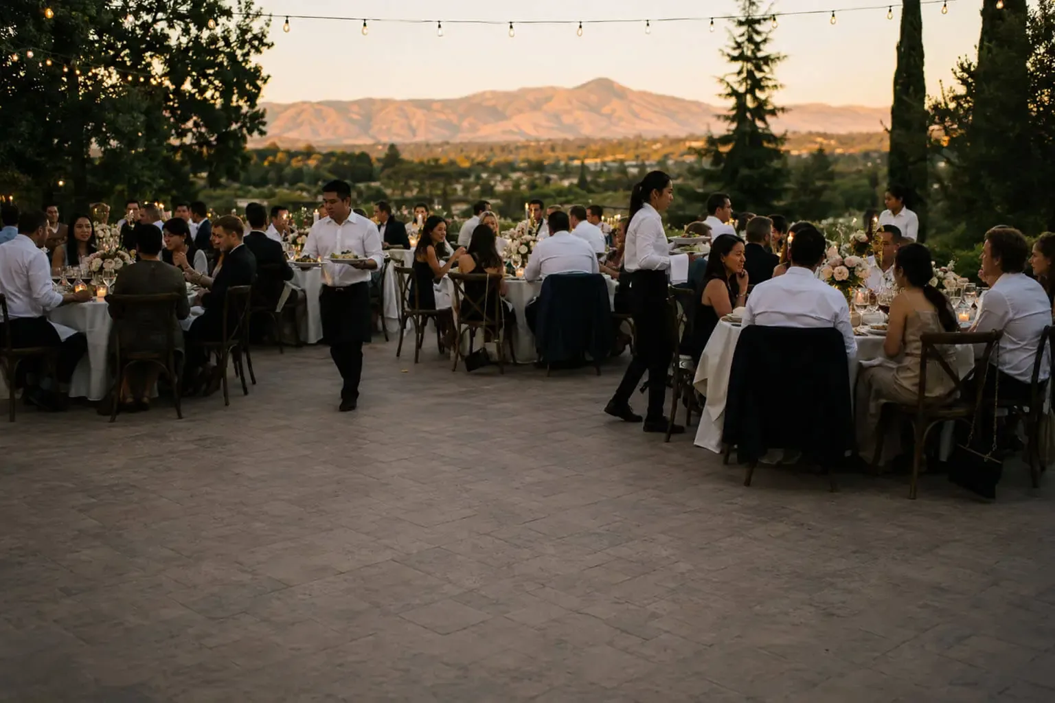 Wedding catering in Fremont, CA by Fremont Catering Company — staffed reception dinner service, rentals, floral tablescapes, cake service and bar service for weddings in Fremont, Newark, Union City, Milpitas and Hayward Outdoor wedding reception at golden hour in Fremont, California — guests seated at linen-draped tables under string lights while catering attendants serve dinner, with Mission Peak and the Tri-City hills behind them
